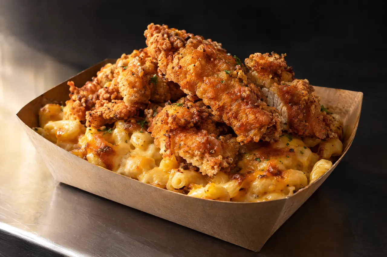 KI-Symbolbild: knuspriges Hähnchen auf Mac and Cheese in einer Pappschale